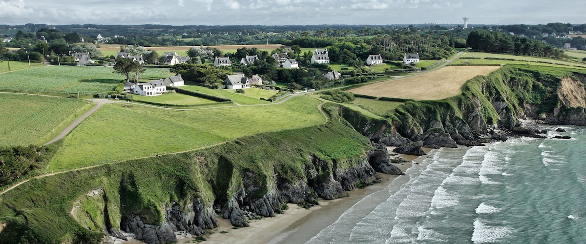 A coastal village with houses on grassy hills, a sandy beach, and the ocean.