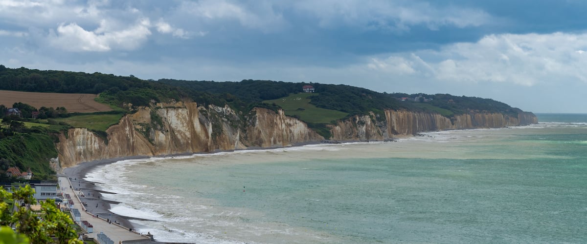 A coastal landscape with cliffs, a beach, and a distant house on a hill.