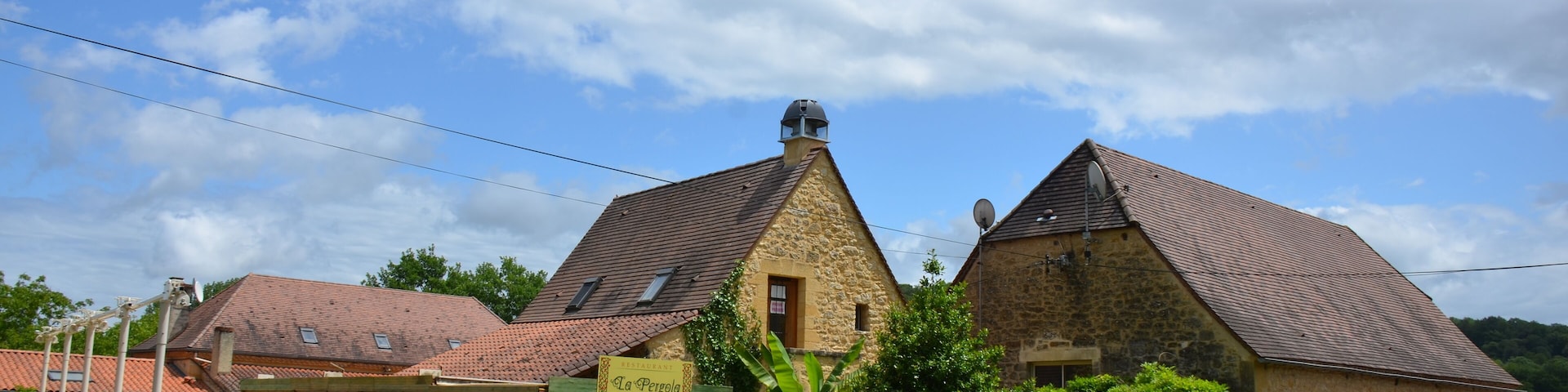 A stone building with a sign reading "La Pergola" and a covered outdoor seating area.