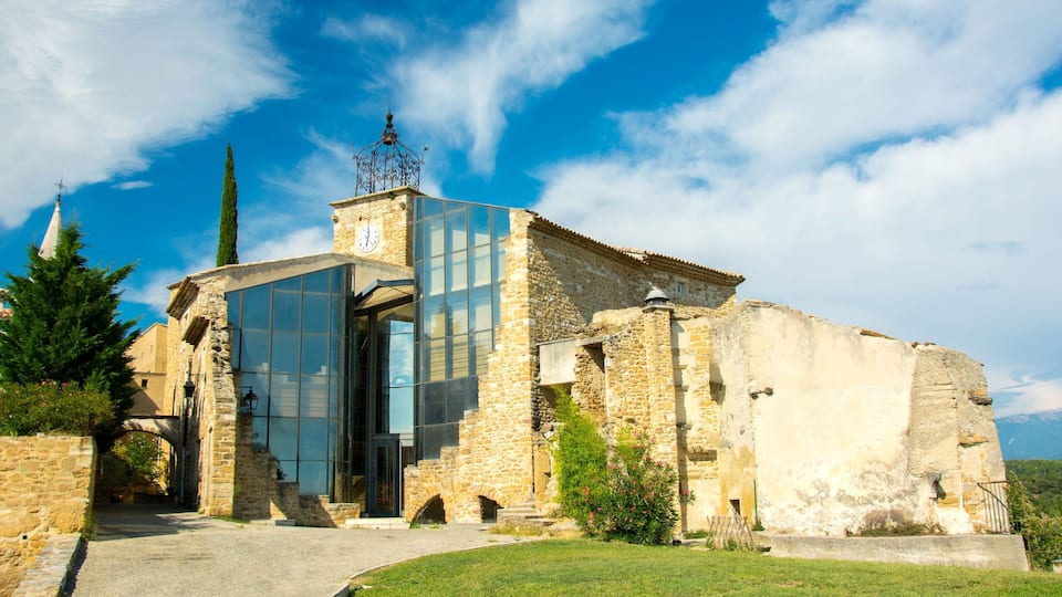 A historic stone church with a modern glass entrance, a bell tower, and a clear blue sky.