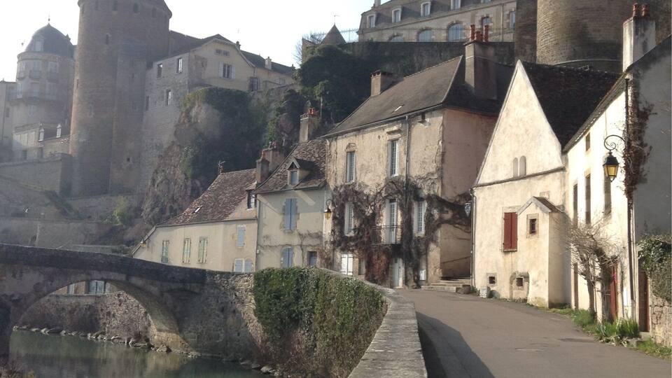 A historic town with a prominent castle on a hill, a stone bridge over a river, and traditional buildings along the riverbank.