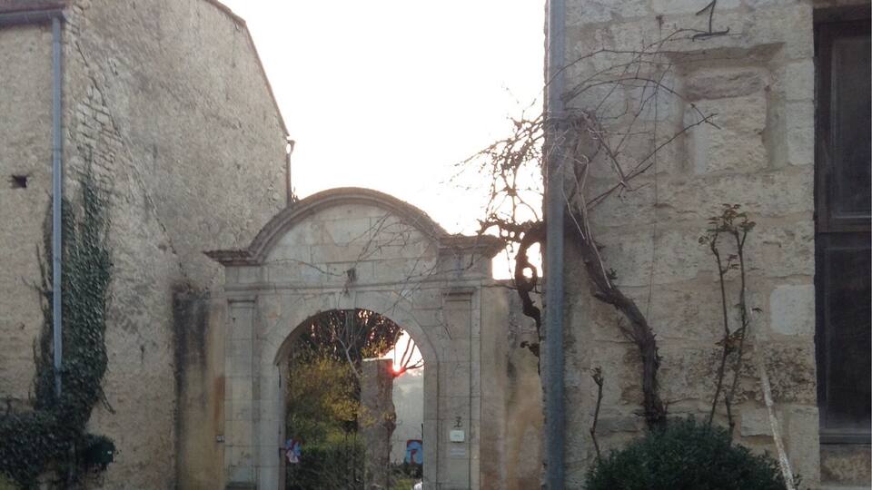 A stone building with a large arched entrance, a dirt path leading to it, and some overgrown vegetation.