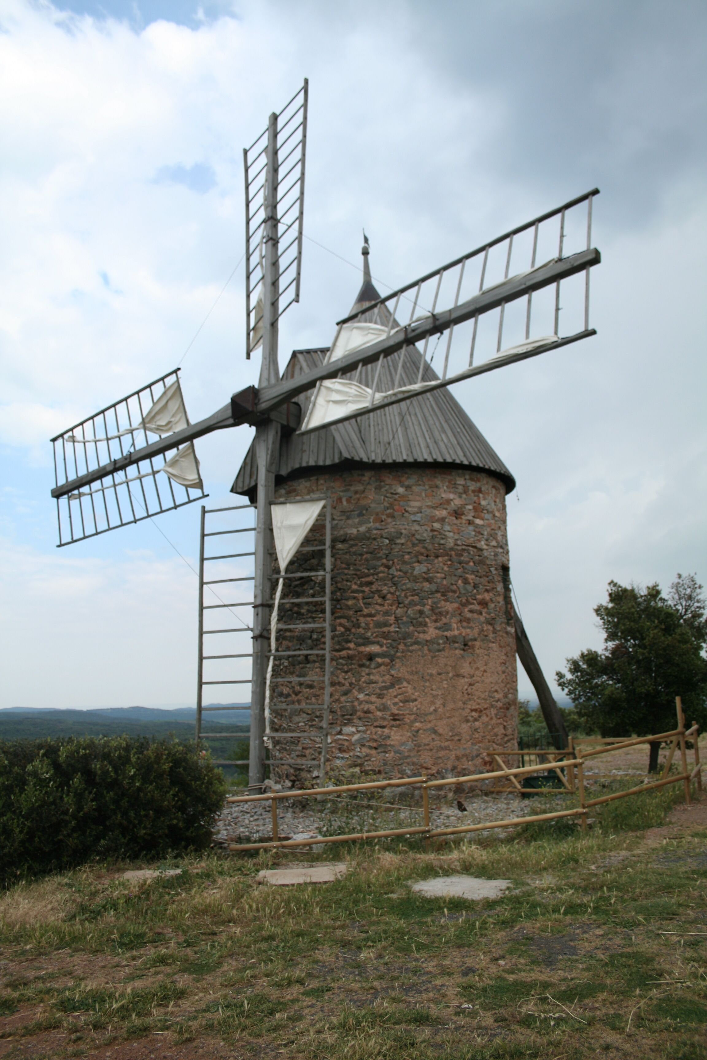 A traditional stone windmill with wooden sails and a metal ladder.