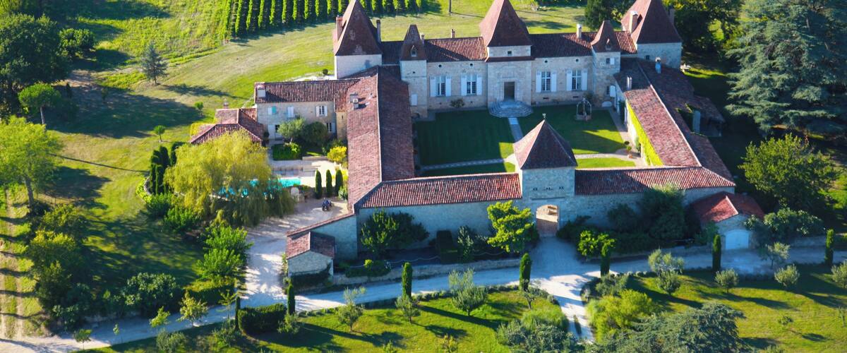 An aerial view of a castle surrounded by neatly arranged vineyards and lush greenery.