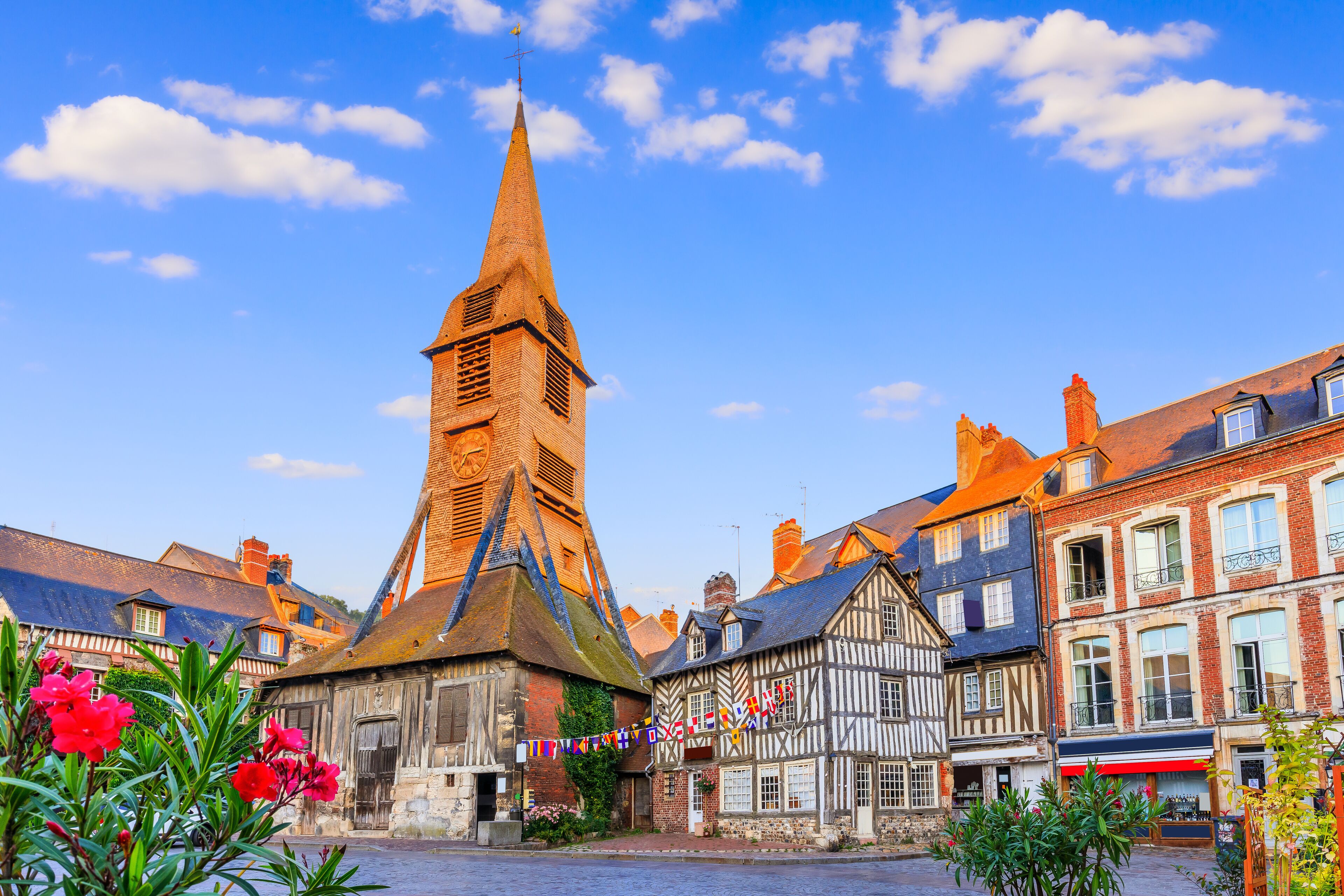 A historic town square with a prominent church tower, traditional half-timbered houses, and cobblestone streets.