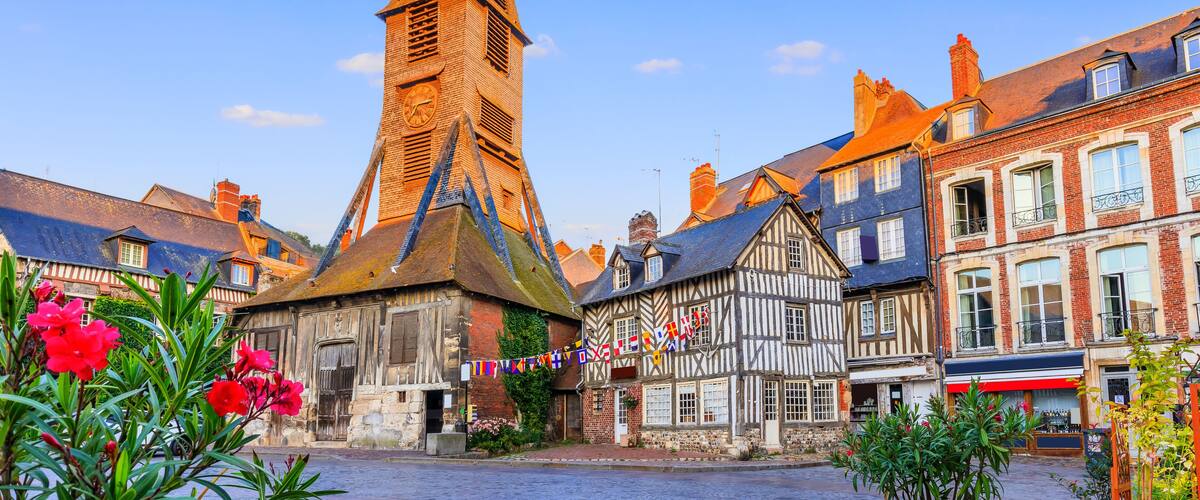 A historic town square with a prominent church tower, traditional half-timbered houses, and cobblestone streets.