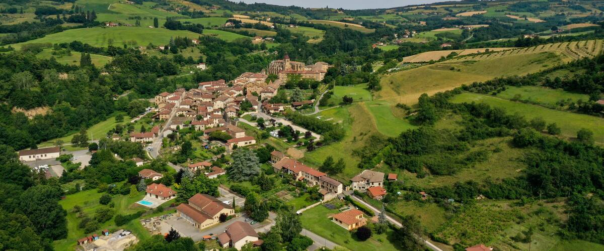 An aerial view of a village with a prominent church, rolling green hills, and scattered houses.