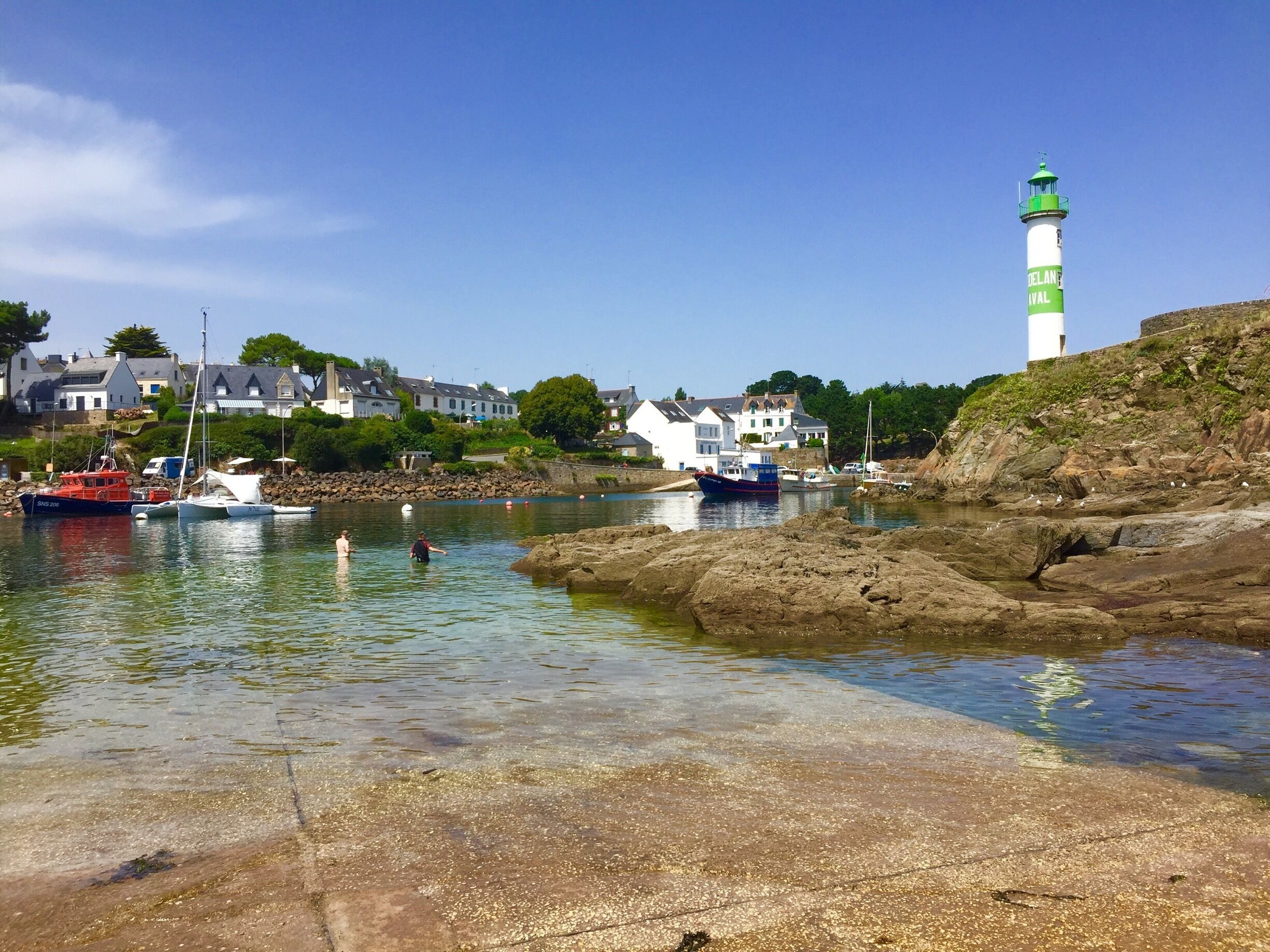 A coastal town with a lighthouse, boats, and houses by the water.