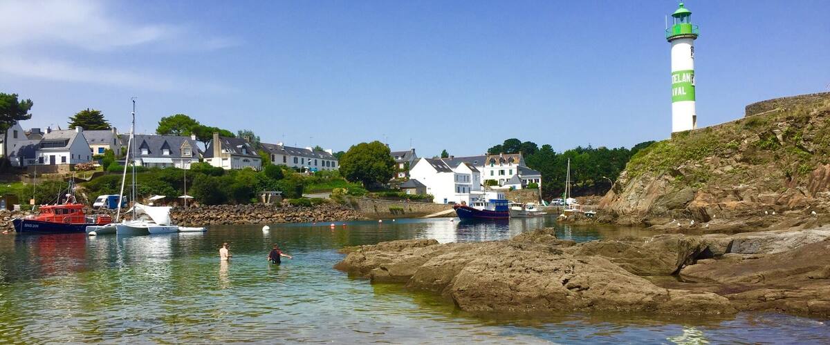 A coastal town with a lighthouse, boats, and houses by the water.