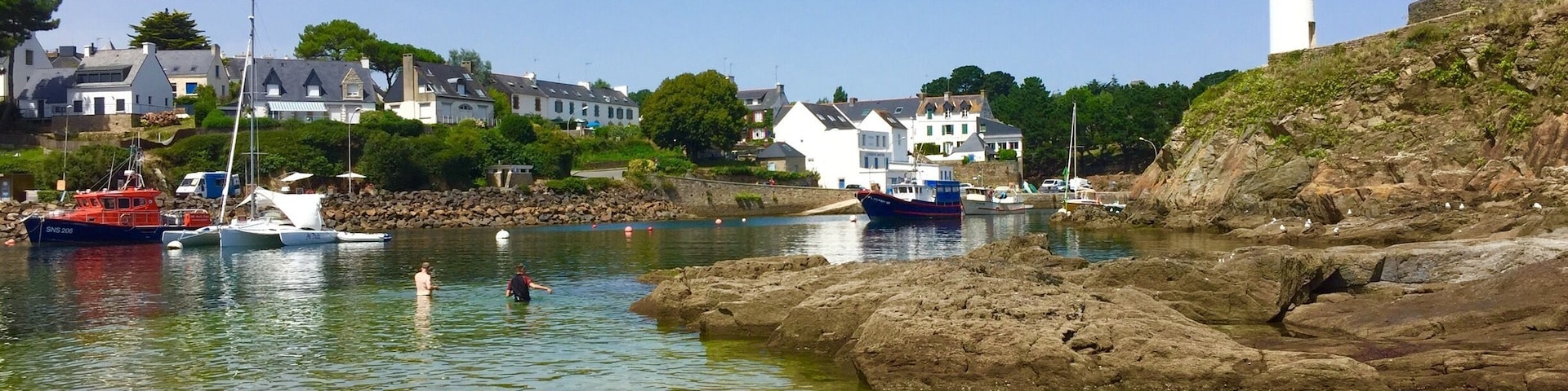 A coastal town with a lighthouse, boats, and houses by the water.