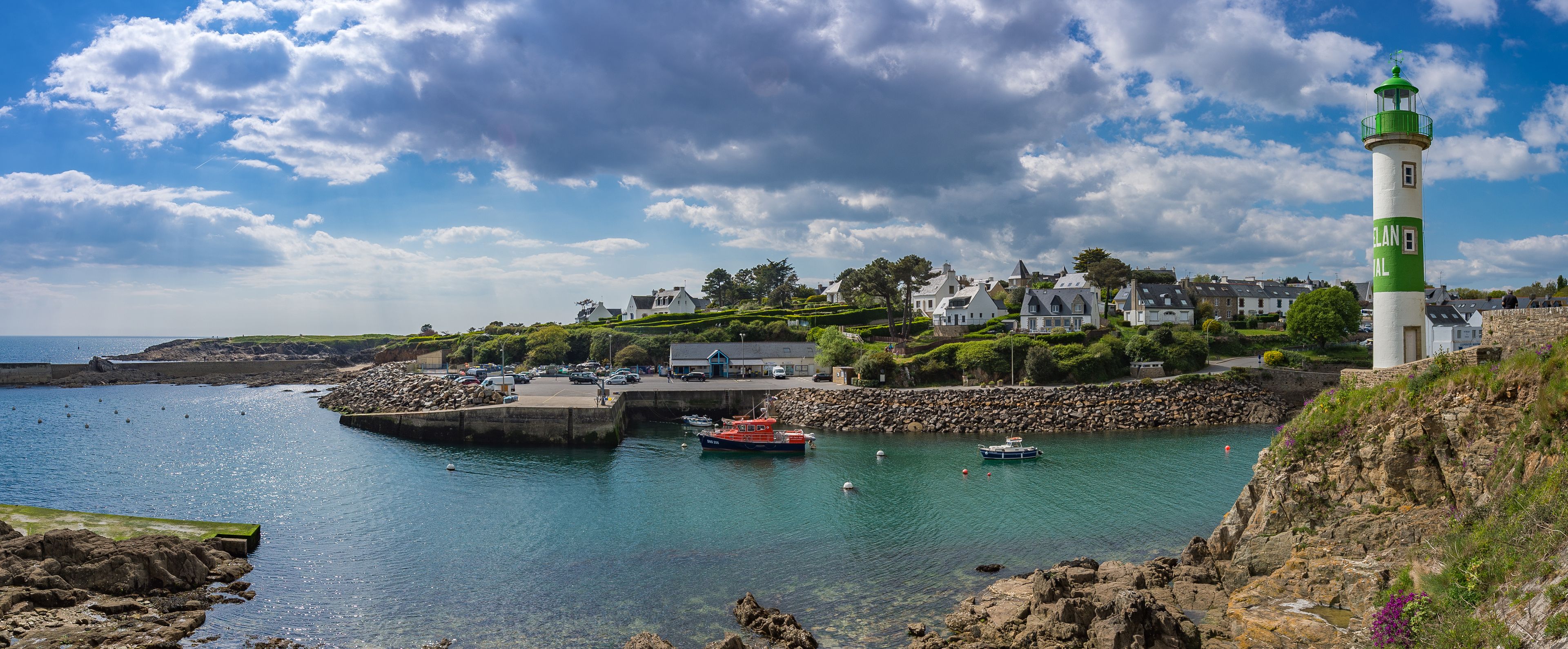 A coastal town with a lighthouse, rocky shoreline, clear blue water, and houses.