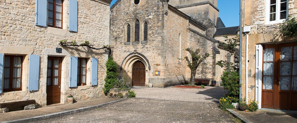 A stone church with a clock tower, a cobblestone street, and traditional shutters on the buildings.