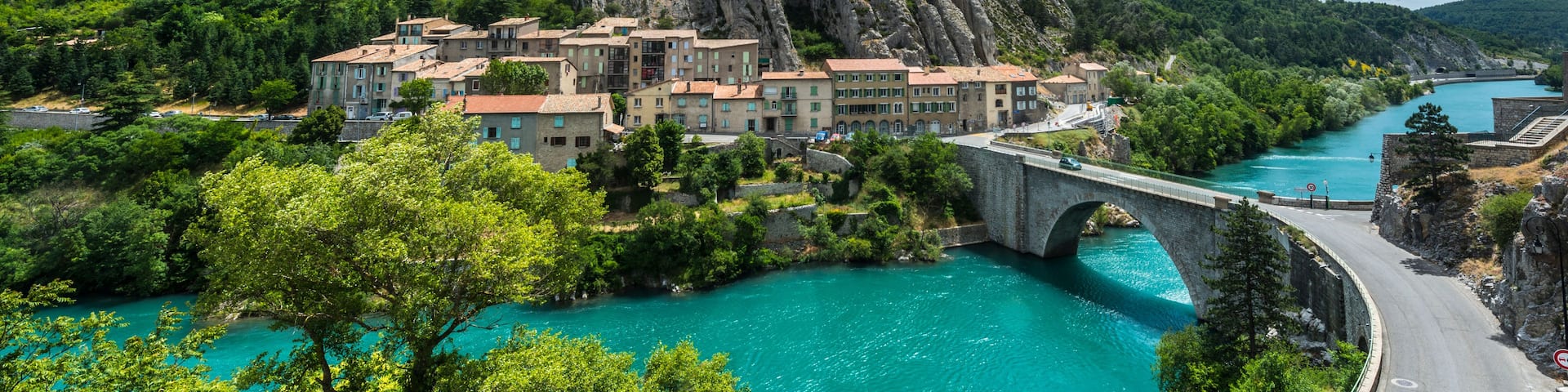 A mountainous landscape with a prominent rocky peak, a bridge, and a river.