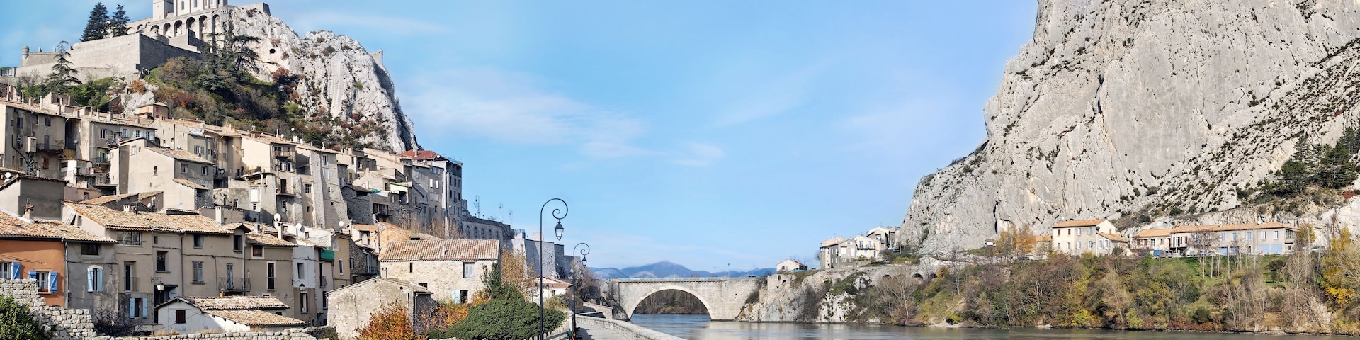 Ein Fluss mit einer Steinbrücke, eine Stadt mit historischen Gebäuden und ein großer Felsabhang.