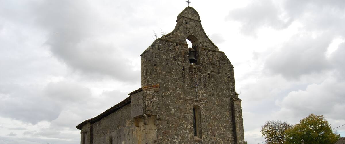 An old stone church with a bell tower and a cross on top.