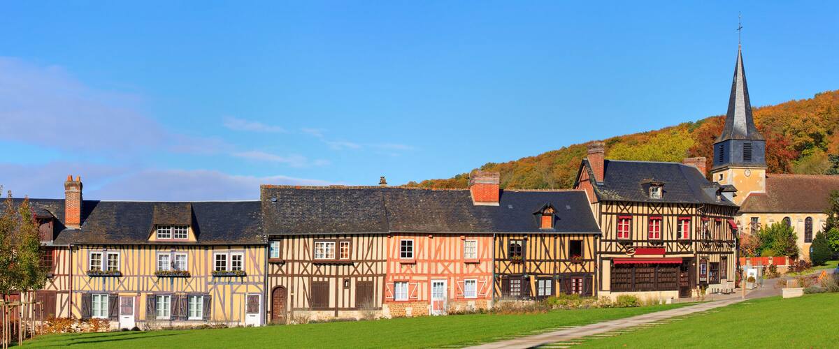 A picturesque village with traditional half-timbered houses, a church with a tall steeple, and a lush green hillside in the background.