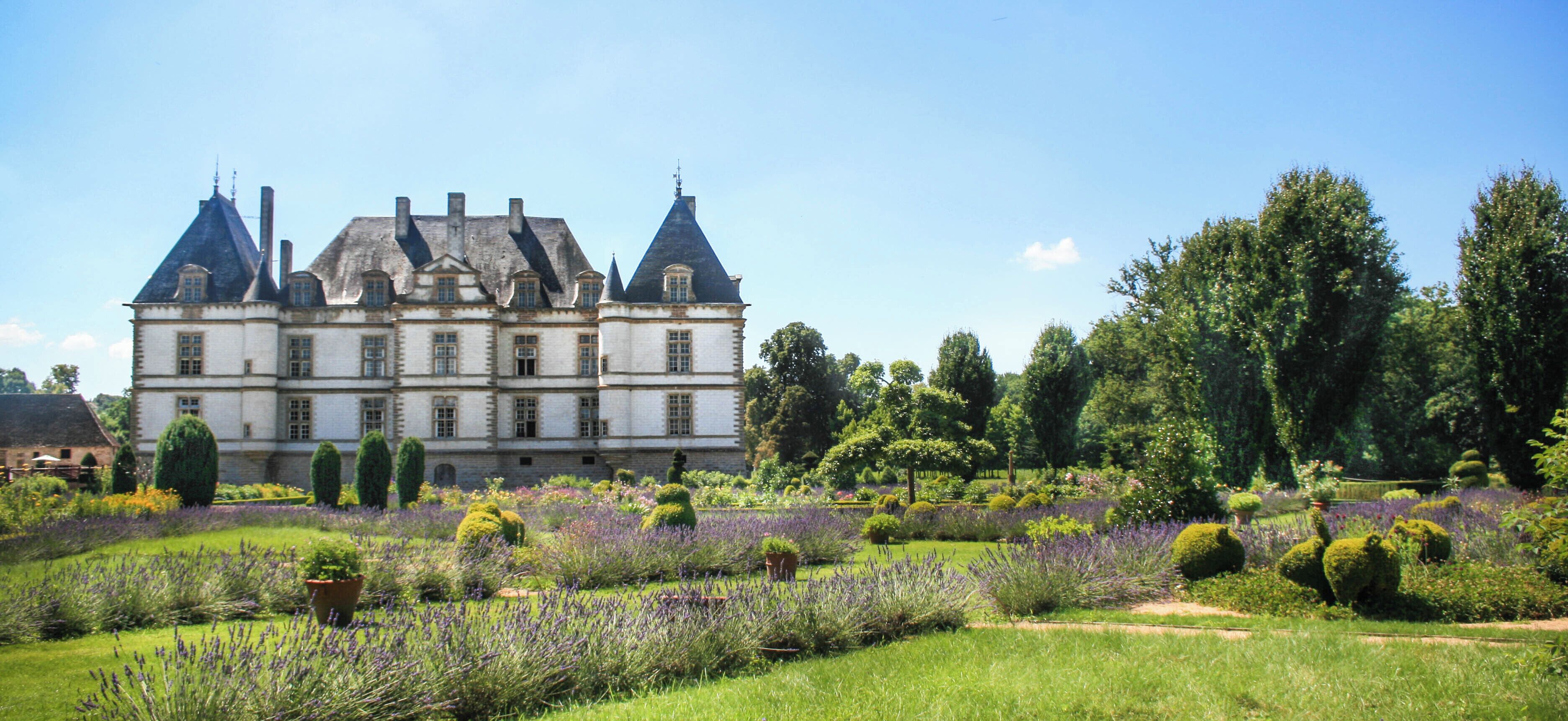 A large, historic building with multiple towers and a well-maintained garden with lavender fields.