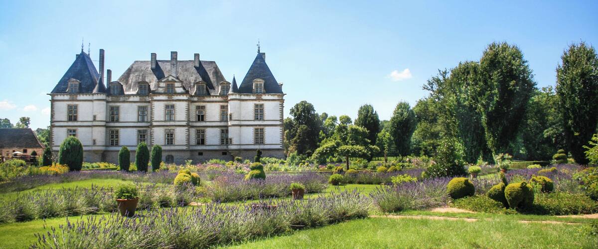 A large, historic building with multiple towers and a well-maintained garden with lavender fields.