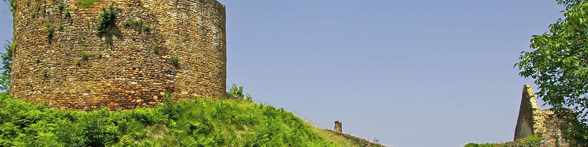 A stone castle ruin on a grassy hill with a bench in the foreground.