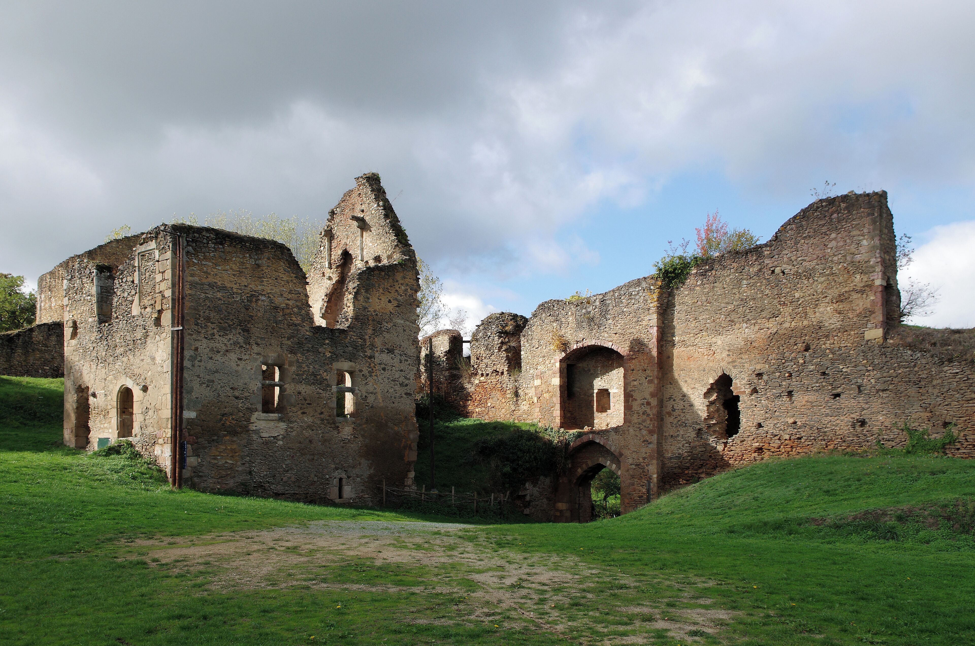 An ancient stone castle with ruins, green grass, and a cloudy sky.