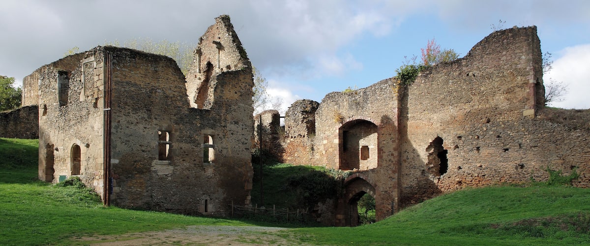 An ancient stone castle with ruins, green grass, and a cloudy sky.