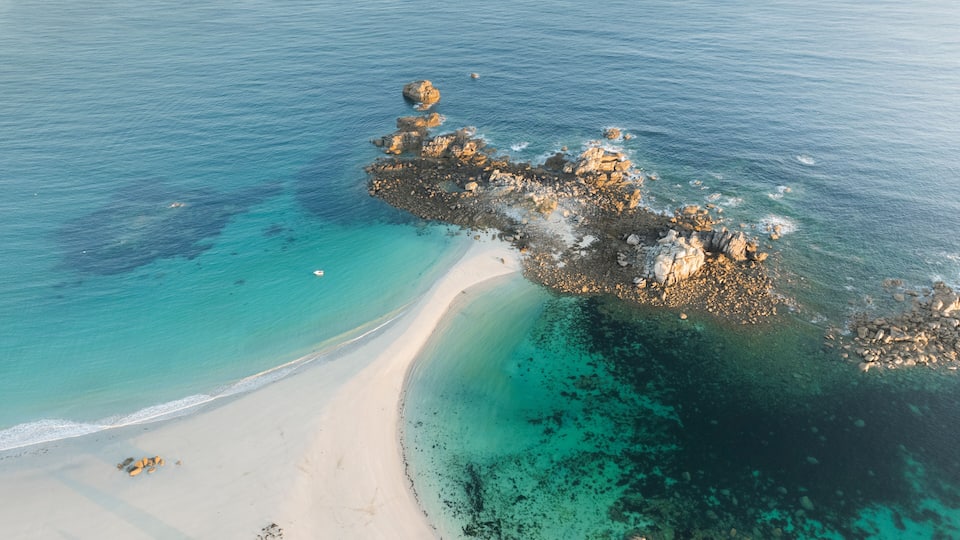 An aerial view of a beach with clear turquoise waters, a sandy shore, and rocky outcrops.