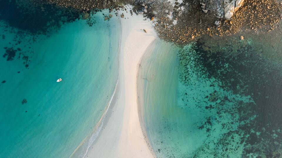 A coastal landscape with a sandy beach, clear turquoise waters, and rocky outcrops.