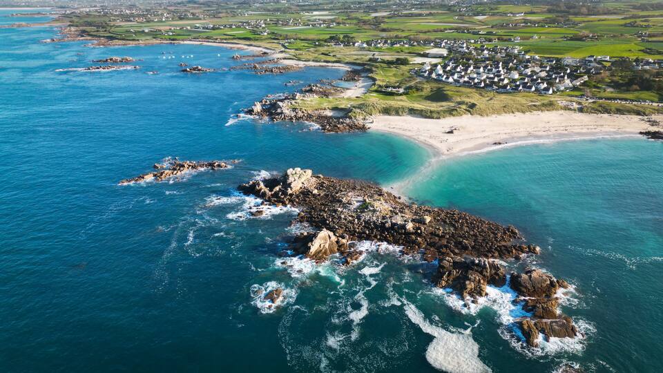 A coastal landscape with rocky outcrops, clear turquoise waters, and a village with white houses.