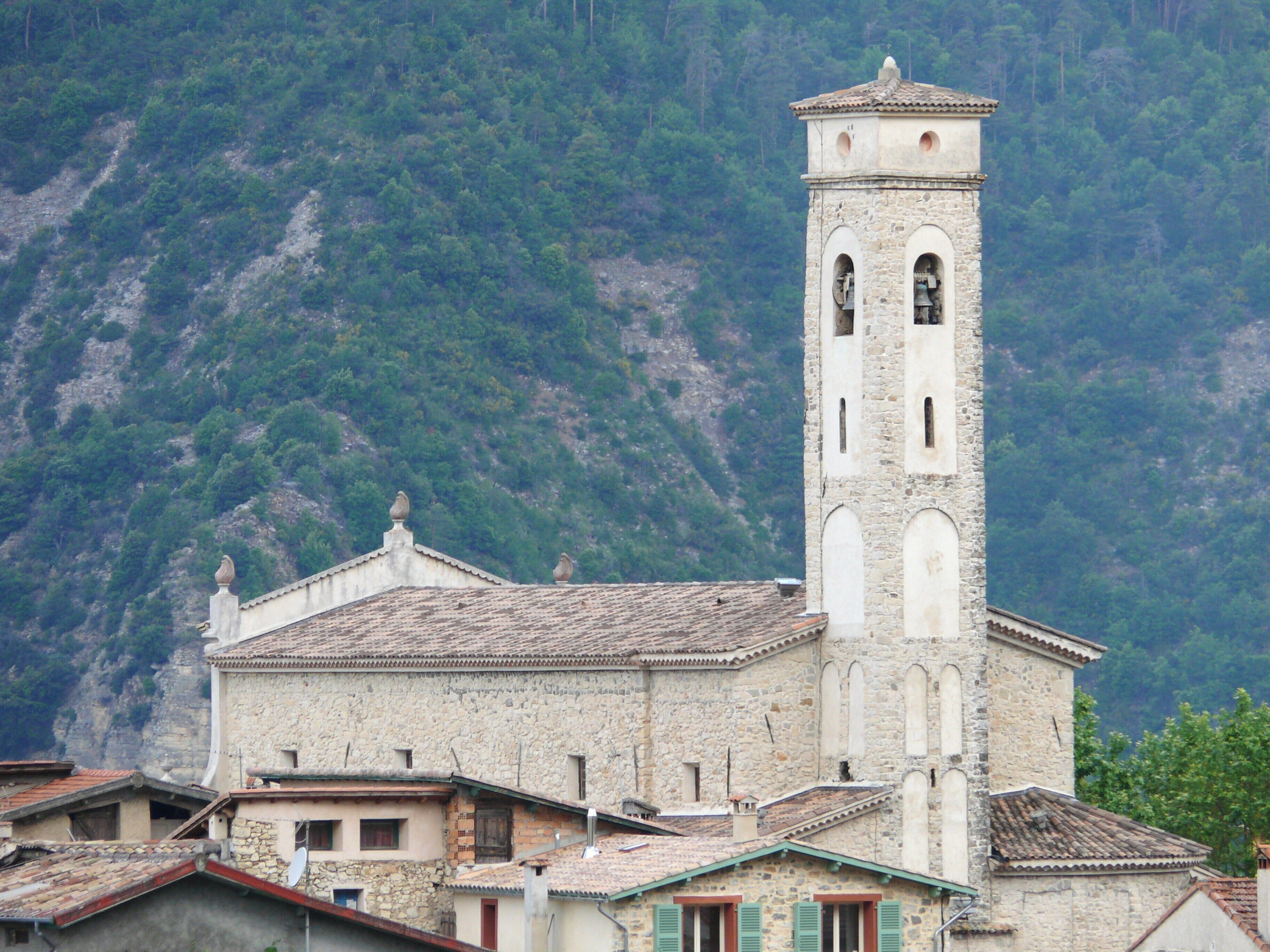A stone church with a bell tower, surrounded by terraced houses and a mountainous backdrop.