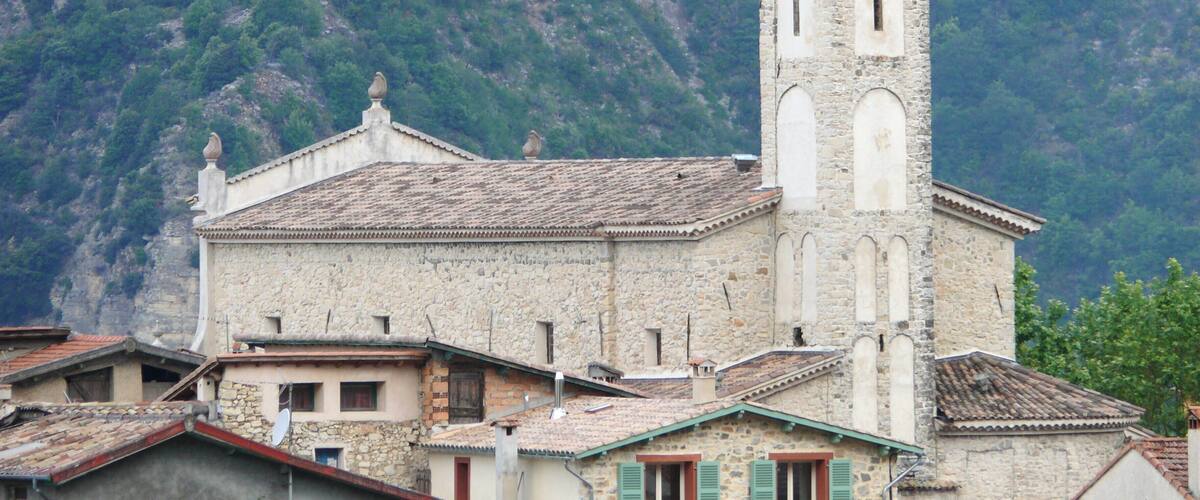 A stone church with a bell tower, surrounded by terraced houses and a mountainous backdrop.