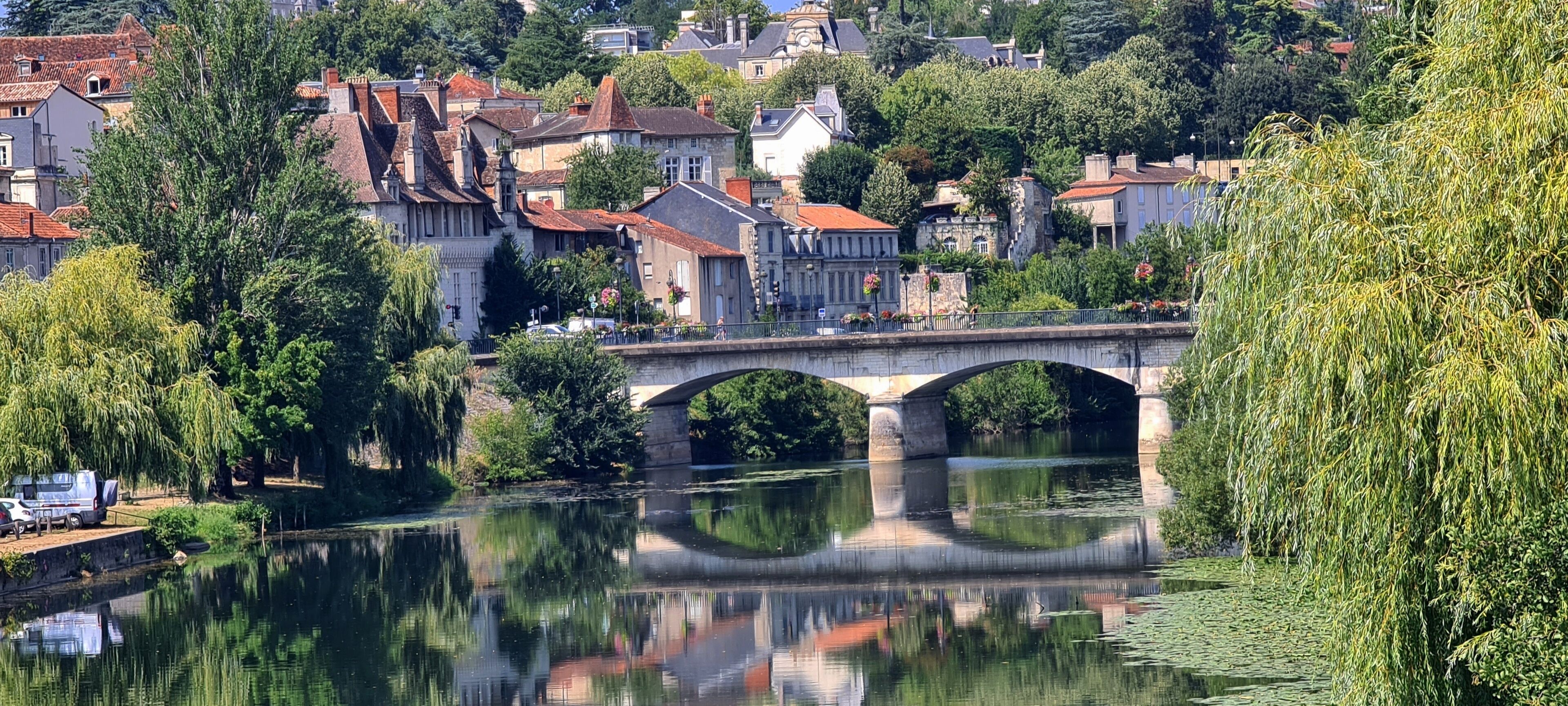 A stone bridge over a calm river, surrounded by lush greenery and historic buildings.