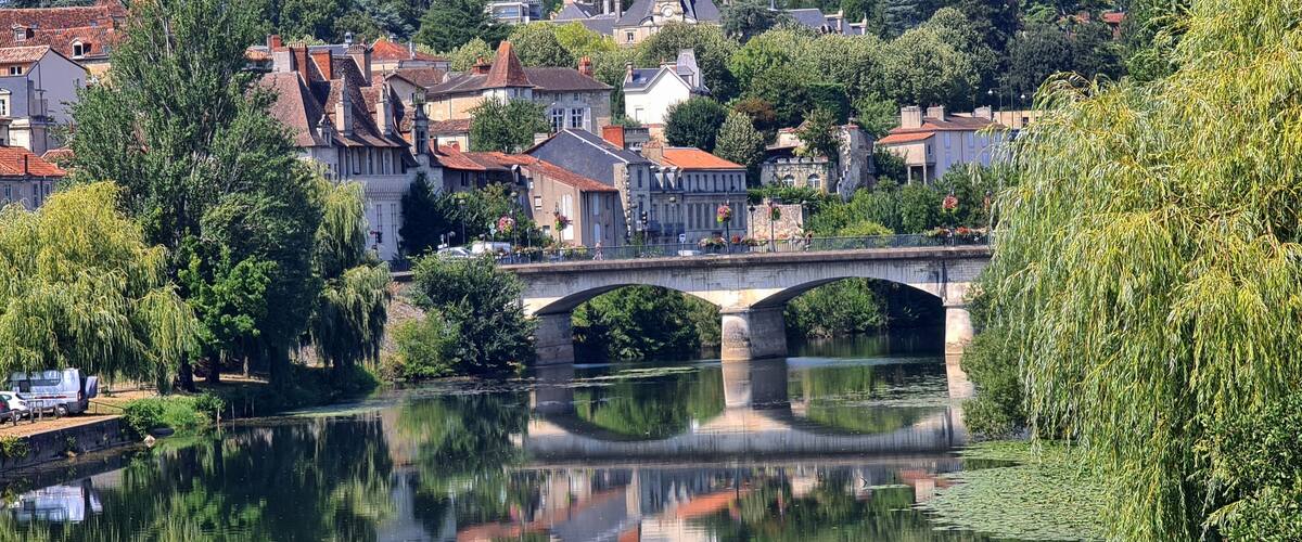 A stone bridge over a calm river, surrounded by lush greenery and historic buildings.