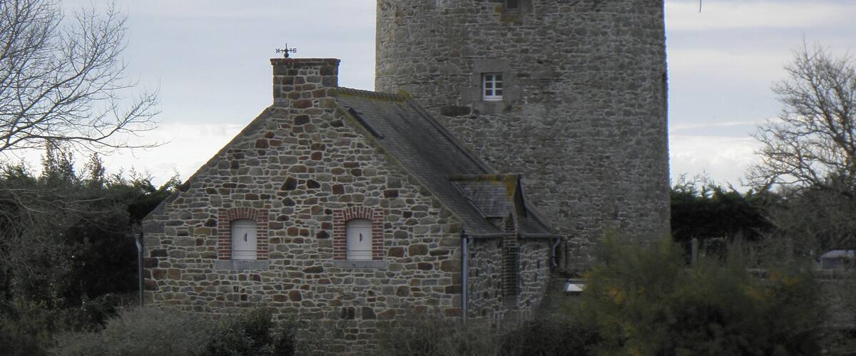 A stone tower with a conical roof and a smaller adjacent building with a gabled roof.