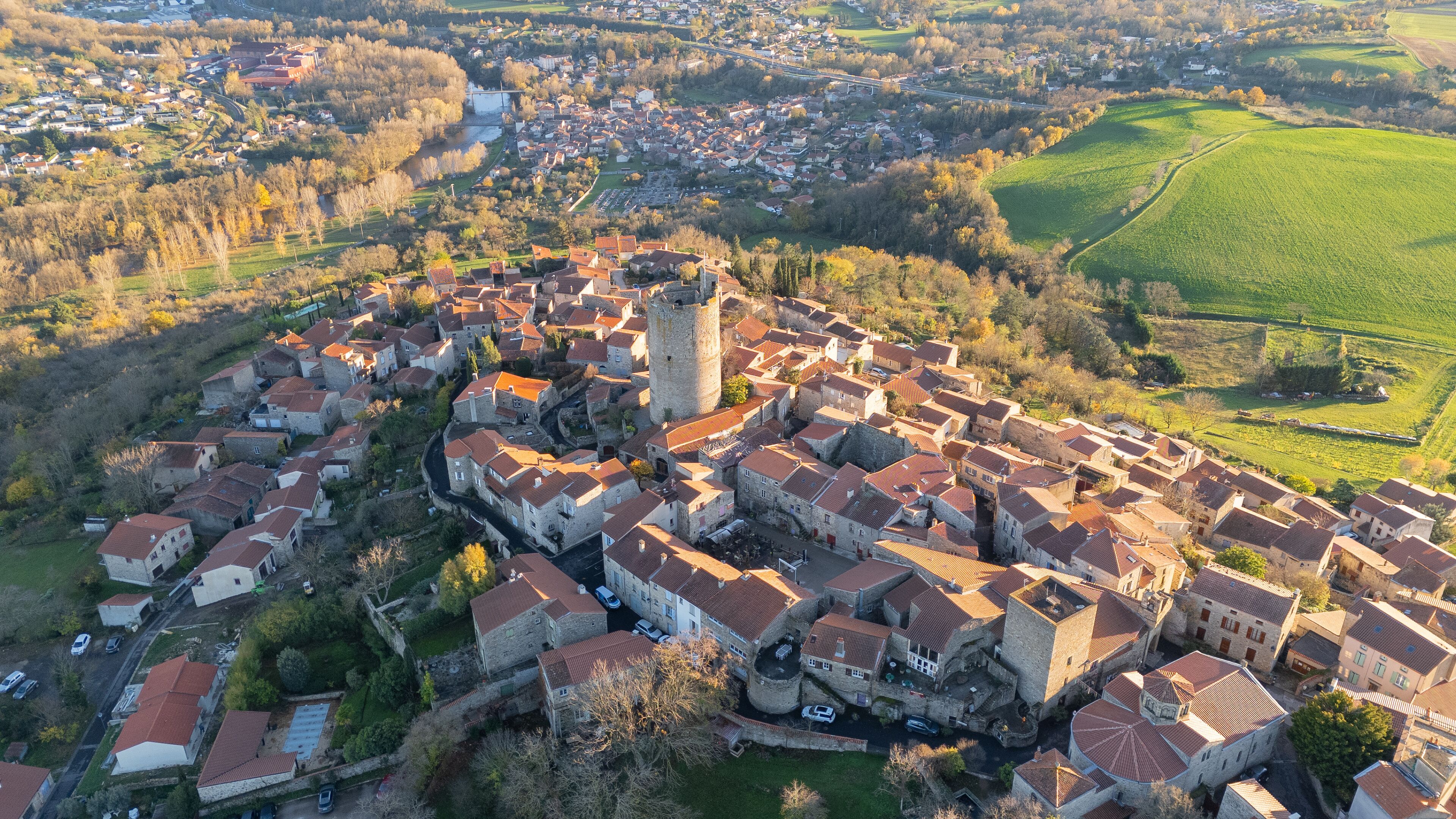 An aerial view of a historic town with a prominent tower, surrounded by lush green fields and a river.
