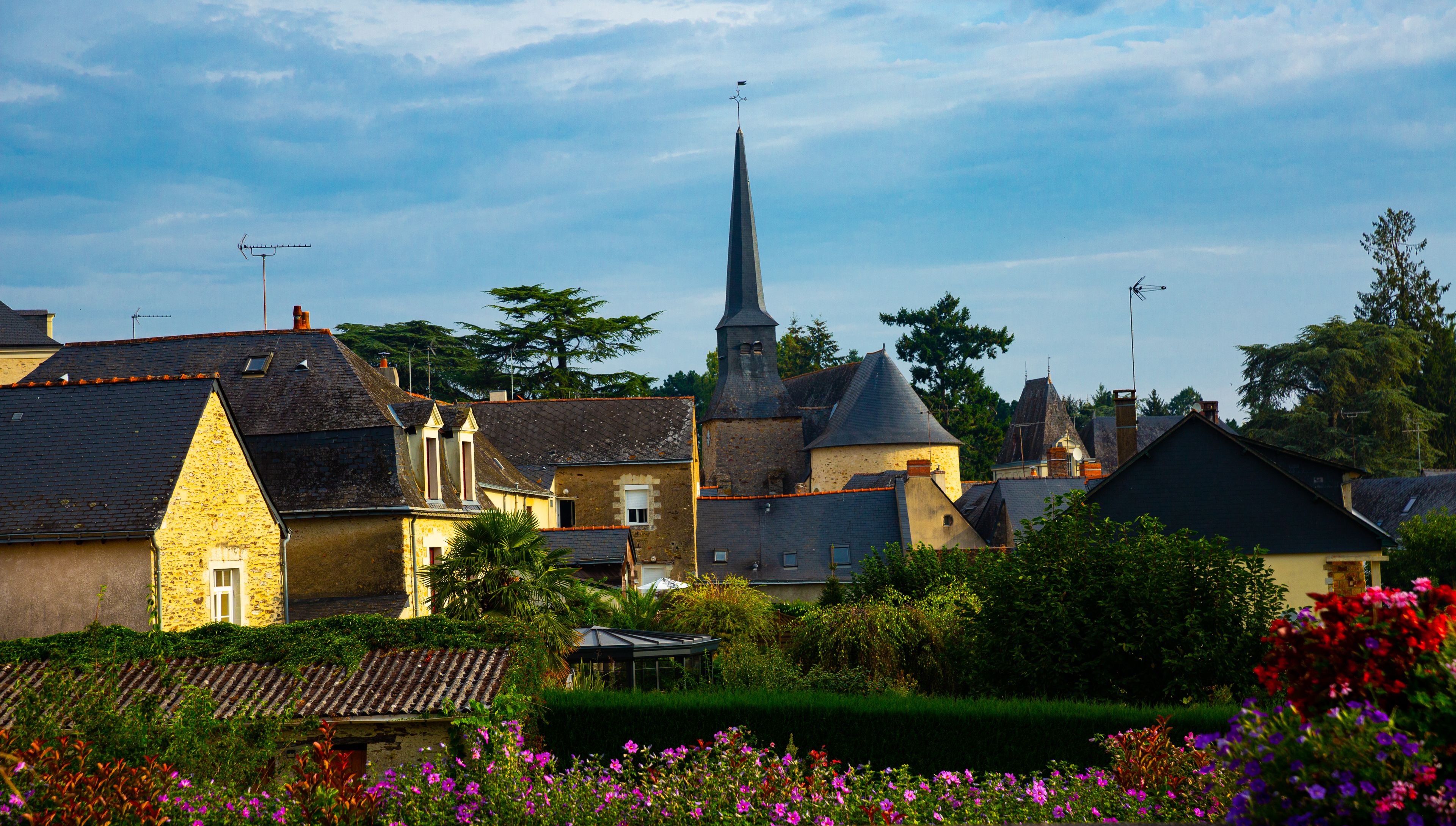 A village with historic buildings, a church spire, and a garden with colorful flowers.