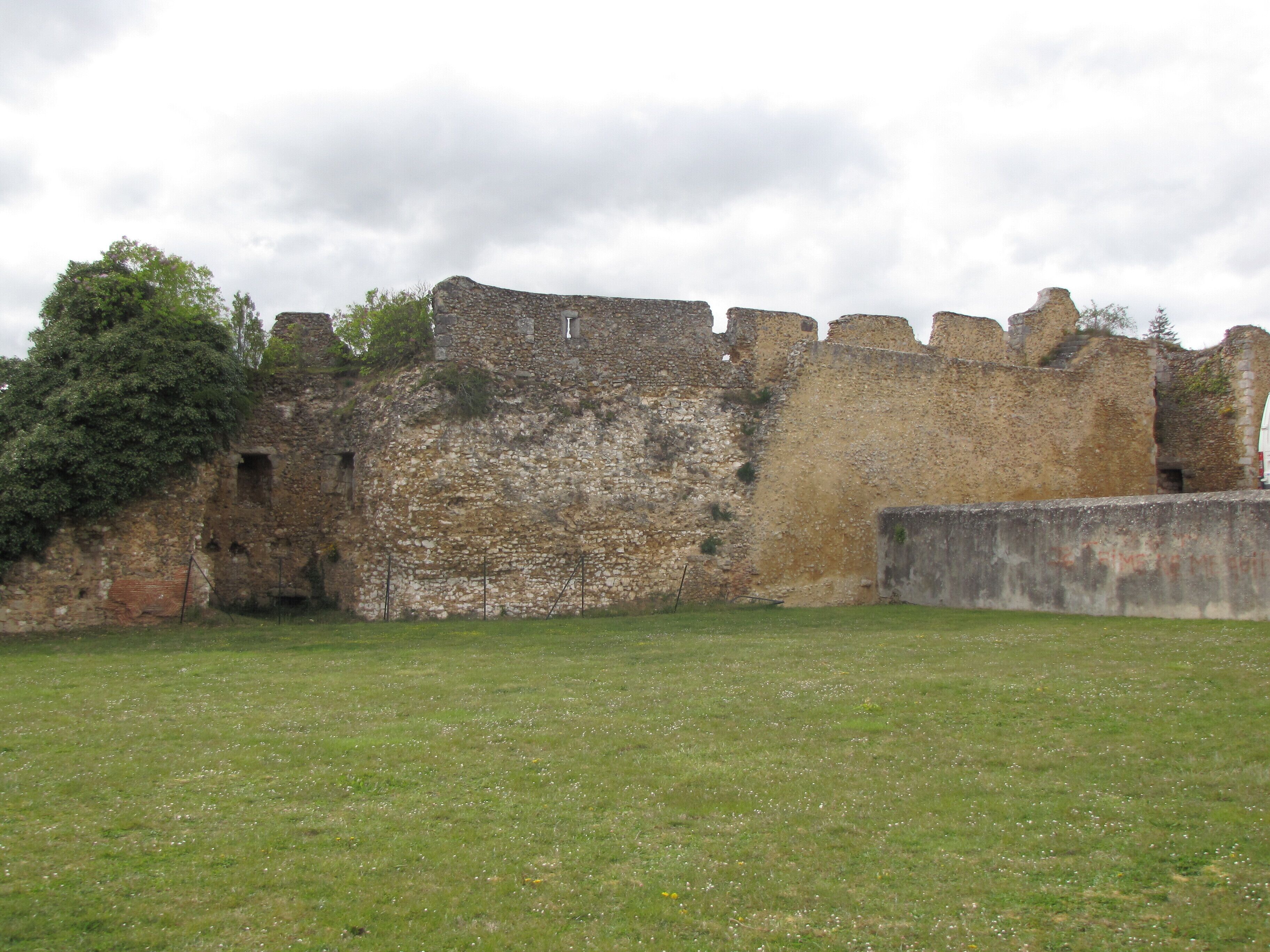 Looking north-west from the center of the panorama place at the château-haut, we see part of the west battlements of the castle. These remnants of fortifications include here two towers and their curtain wall, with part of the chemin de ronde and some crenels. The red gate leading downtown is immediately after the tower on the right The tower on the left still shows the holes in which were set the beams supporting a floor. Their height, or lack thereof, tells that the actual ground of the inner courtyard was quite a way deeper than it is now. On the left hand-side of the same tower, the wall shows some brickwork that tells of a door, now walled-in and nearly buried.