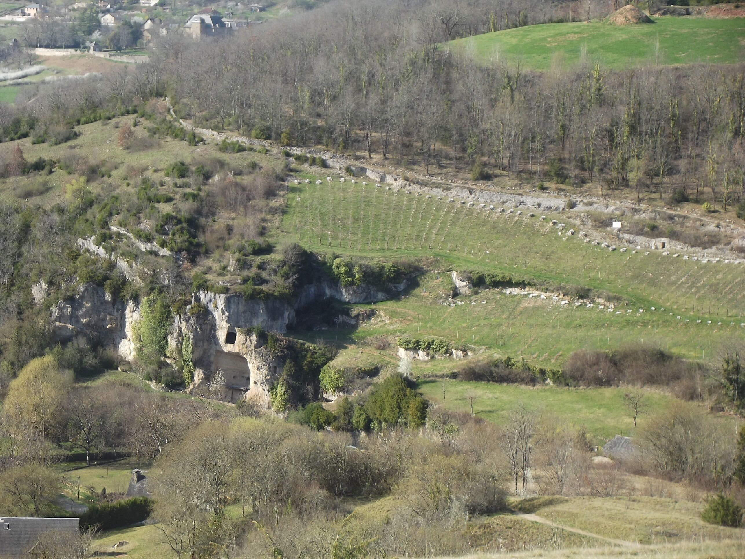 A rural landscape with terraced fields, rocky outcrops, and scattered trees.