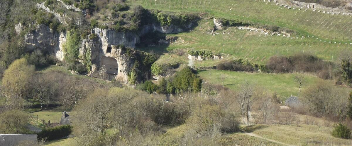 A rural landscape with terraced fields, rocky outcrops, and scattered trees.