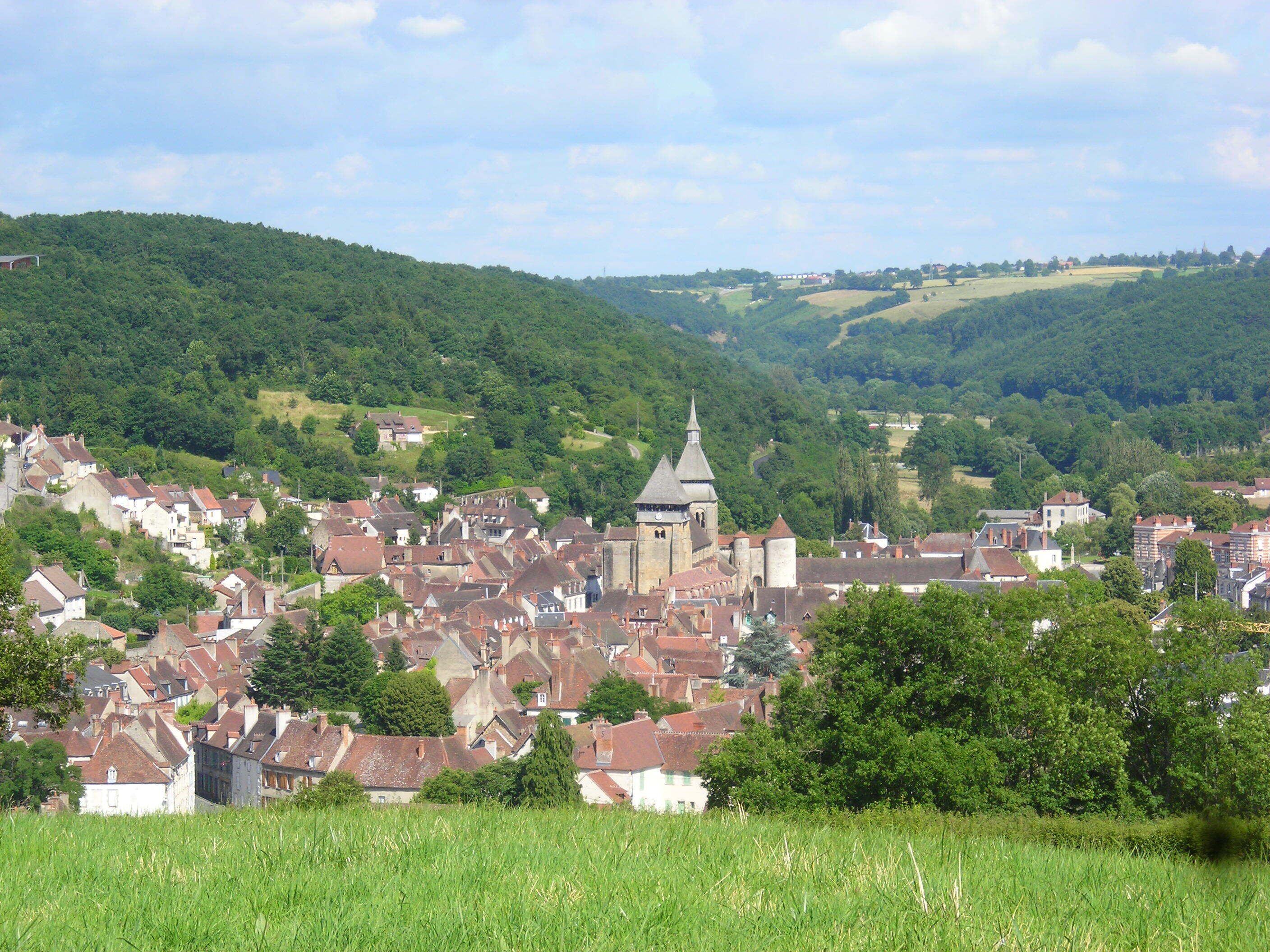 A historic town with a prominent church tower, surrounded by lush green hills and residential buildings.