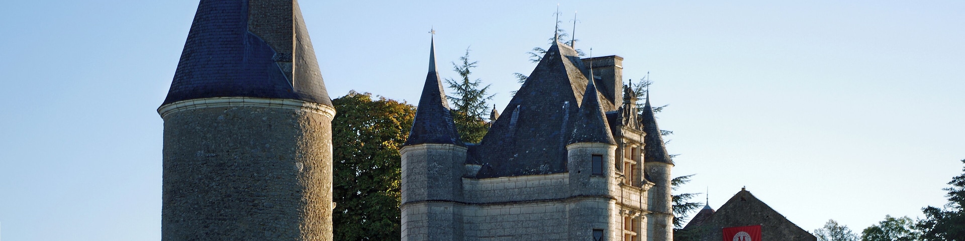 Un castillo histórico con una torre alta y un edificio más pequeño con un estandarte rojo.