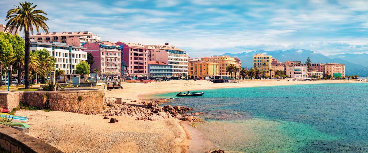 A coastal cityscape with a sandy beach, colorful buildings, and mountains in the background.