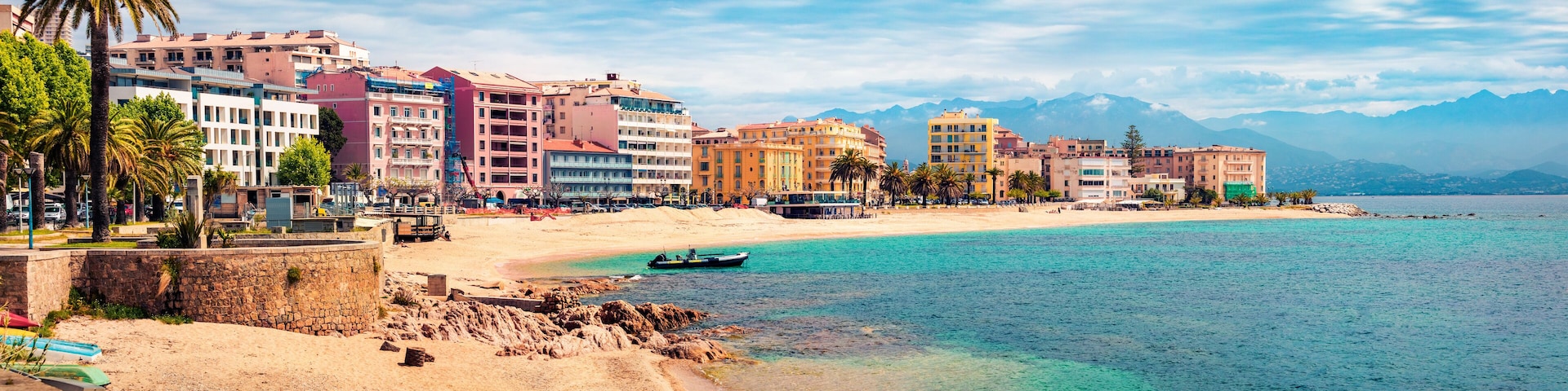 A coastal cityscape with a sandy beach, colorful buildings, and mountains in the background.