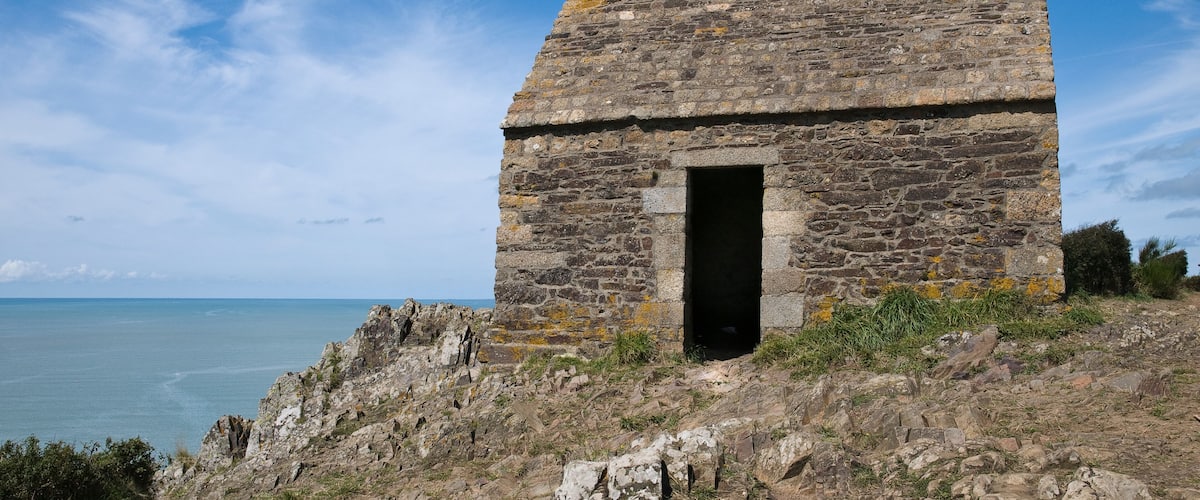A stone structure with a door, overlooking a coastal landscape.