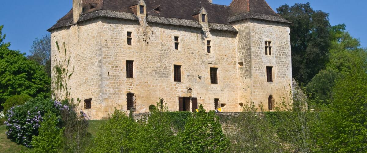 A historic stone castle with multiple towers and windows, surrounded by lush greenery.