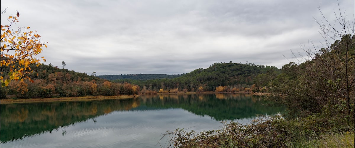 A calm lake surrounded by autumn-colored trees and a hill in the distance.