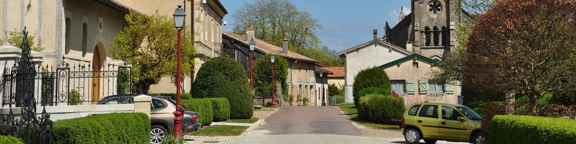 A village street with a church tower, residential buildings, and a car parked on the side.