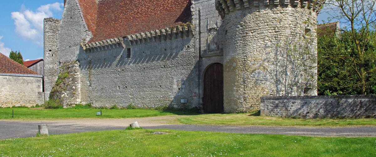 A historic stone building with a red-tiled roof and a round tower.