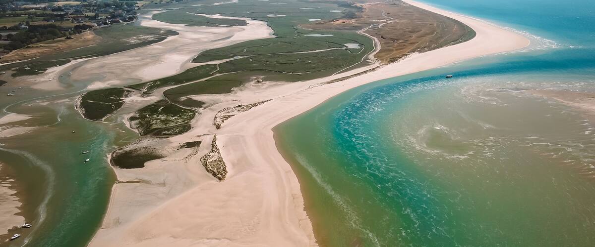 An aerial view of a coastal area with a sandy beach, clear blue waters, and a river delta.