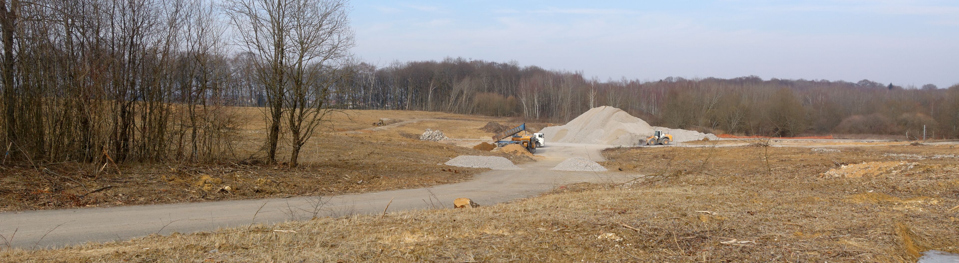 A construction site with a pile of gravel and a dirt road.