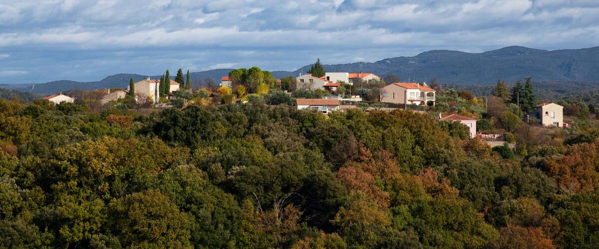 A hillside village with houses, trees, and mountains in the background.
